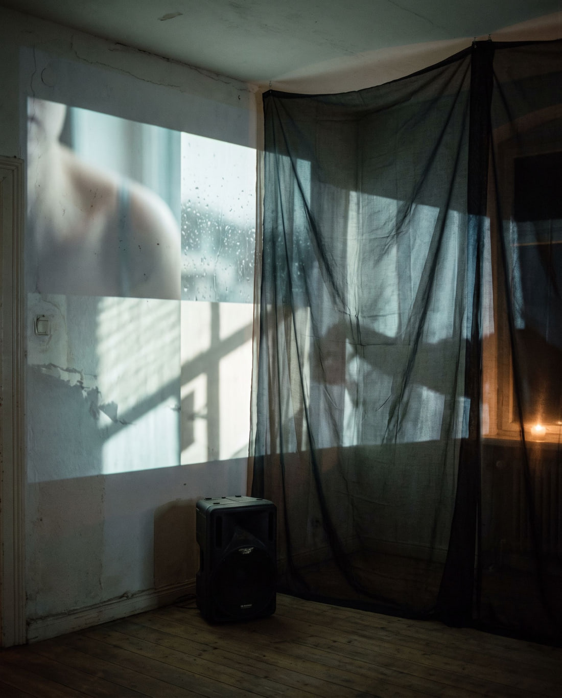 Projected audiovisual image falling across a worn wall and translucent fabric in a dark room.