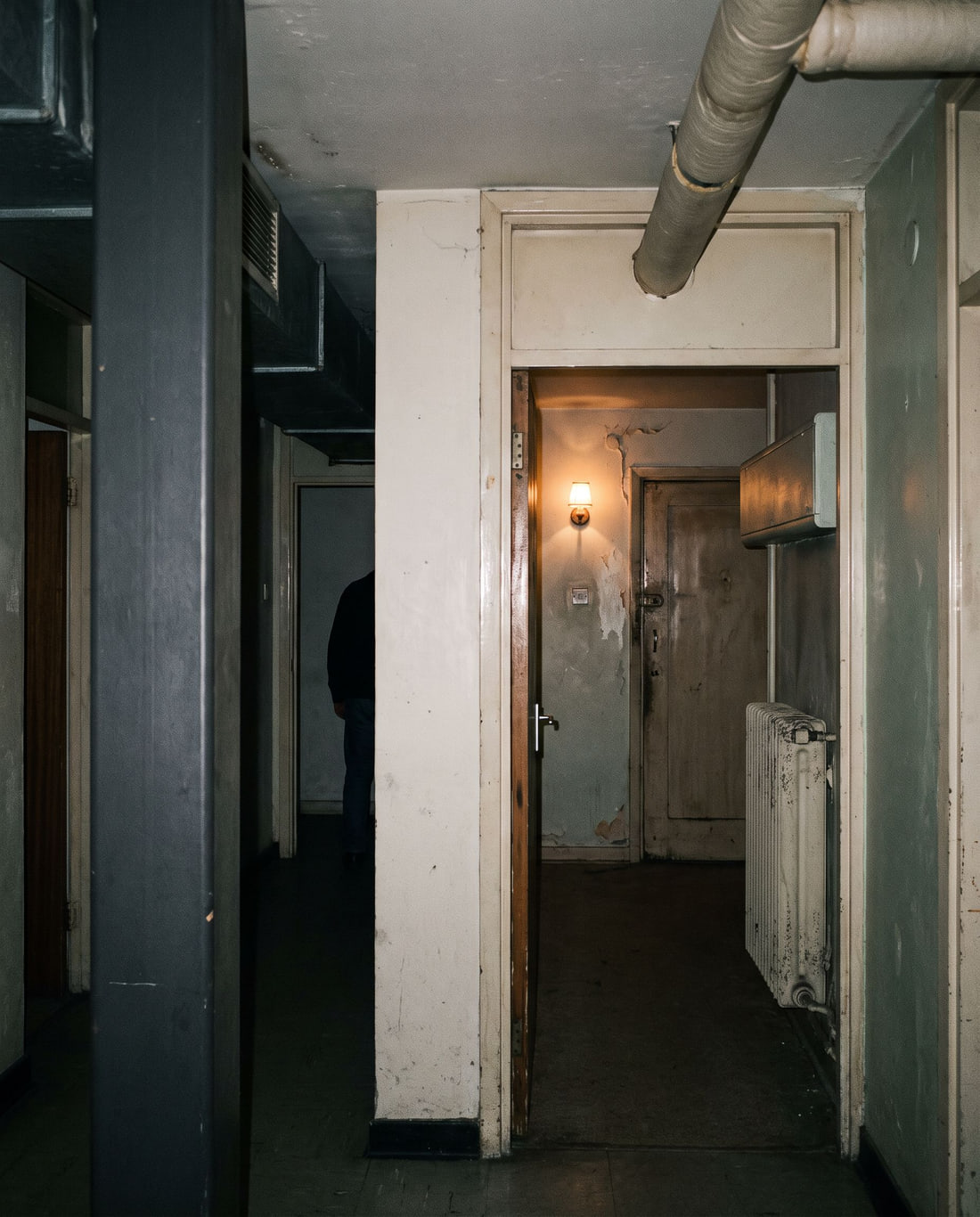 Domestic interior progressively occupied by technical architecture, with a small distant figure.